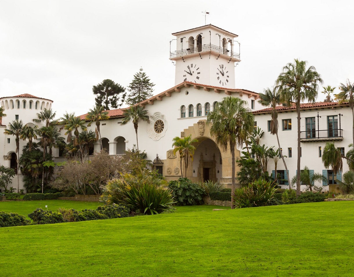 Santa Barbara Courthouse with white stucco walls, red-tiled roof, clock tower, and palm trees in a landscaped garden.