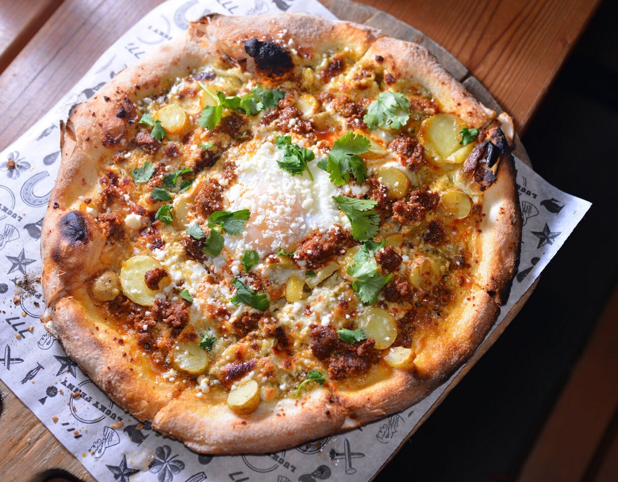 Wood-fired pizza with sliced potatoes, herbs, cheese, and spices on decorative paper.