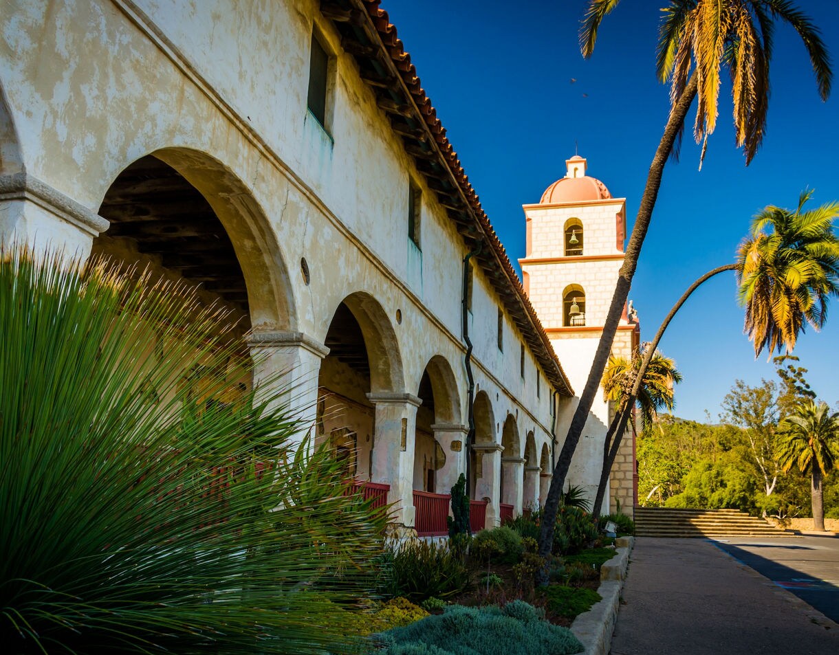 White Spanish Colonial Revival courthouse building with bell tower, arched entrance, and palm trees under blue sky.