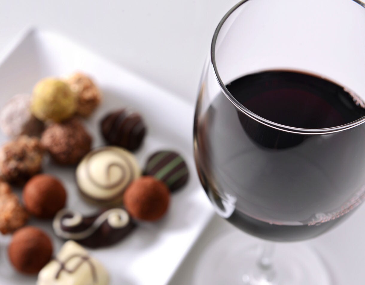 A glass of red wine next to a plate of assorted gourmet chocolates and truffles.