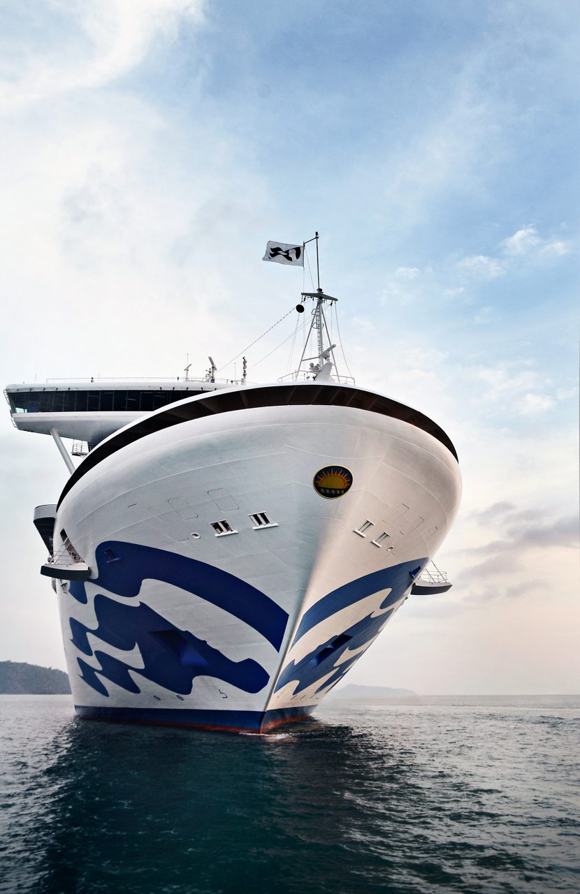 Close-up of the Sapphire Princess cruise ship sailing on calm waters, with its sleek design and iconic Princess Cruises logo visible on the hull, set against a serene sunset sky.