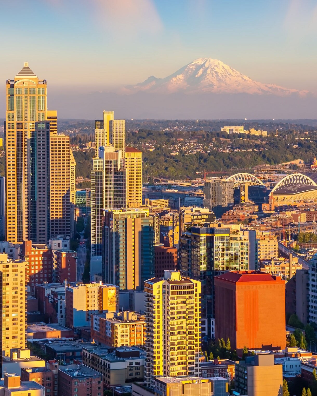 Downtown Seattle high-rises lit by golden hour with snow-capped Mount Rainier behind the city.