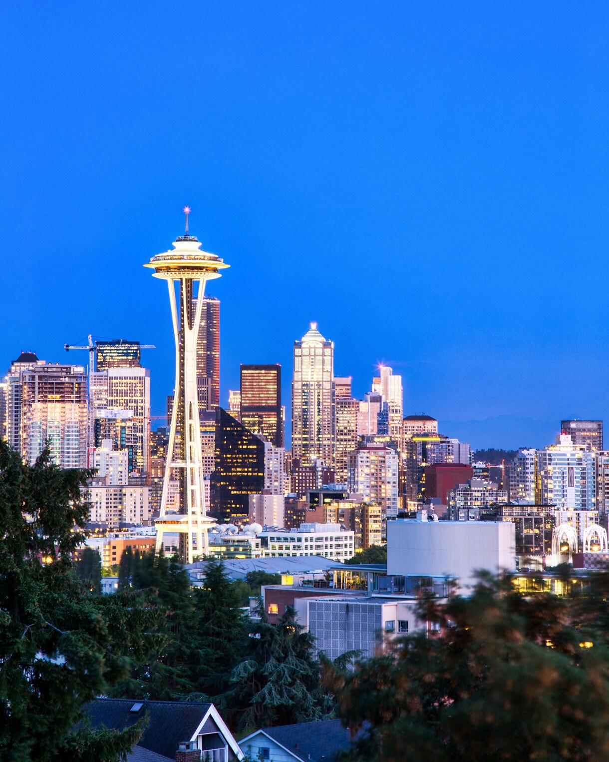 Seattle skyline at dusk with the illuminated Space Needle rising above downtown buildings.