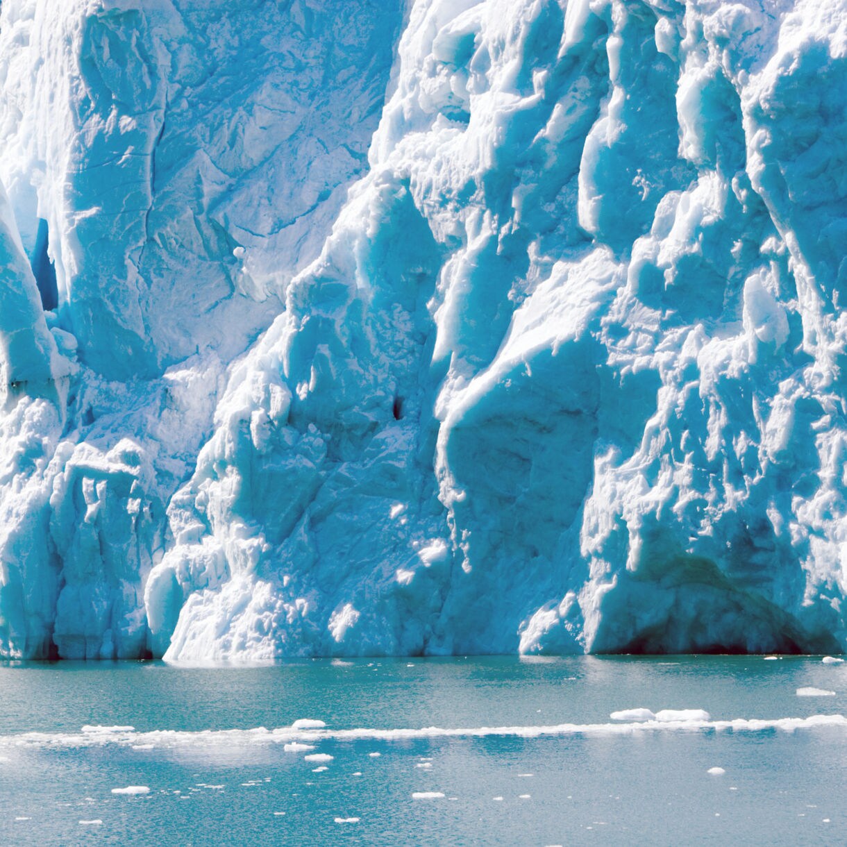 Massive glacier face near Seward, Alaska with jagged blue ice formations and floating ice chunks on the surface of calm, cold water.