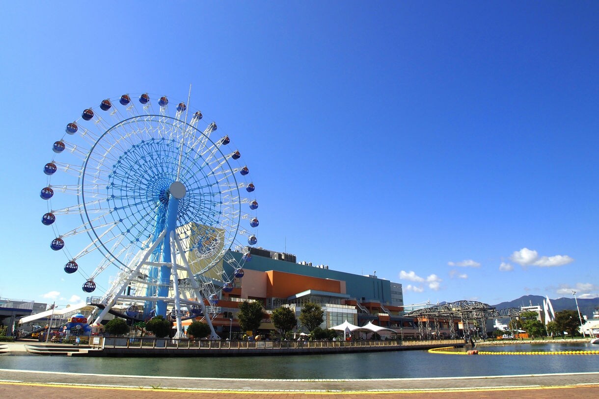 Large Ferris wheel beside a colorful waterfront shopping and entertainment complex under a clear blue sky.