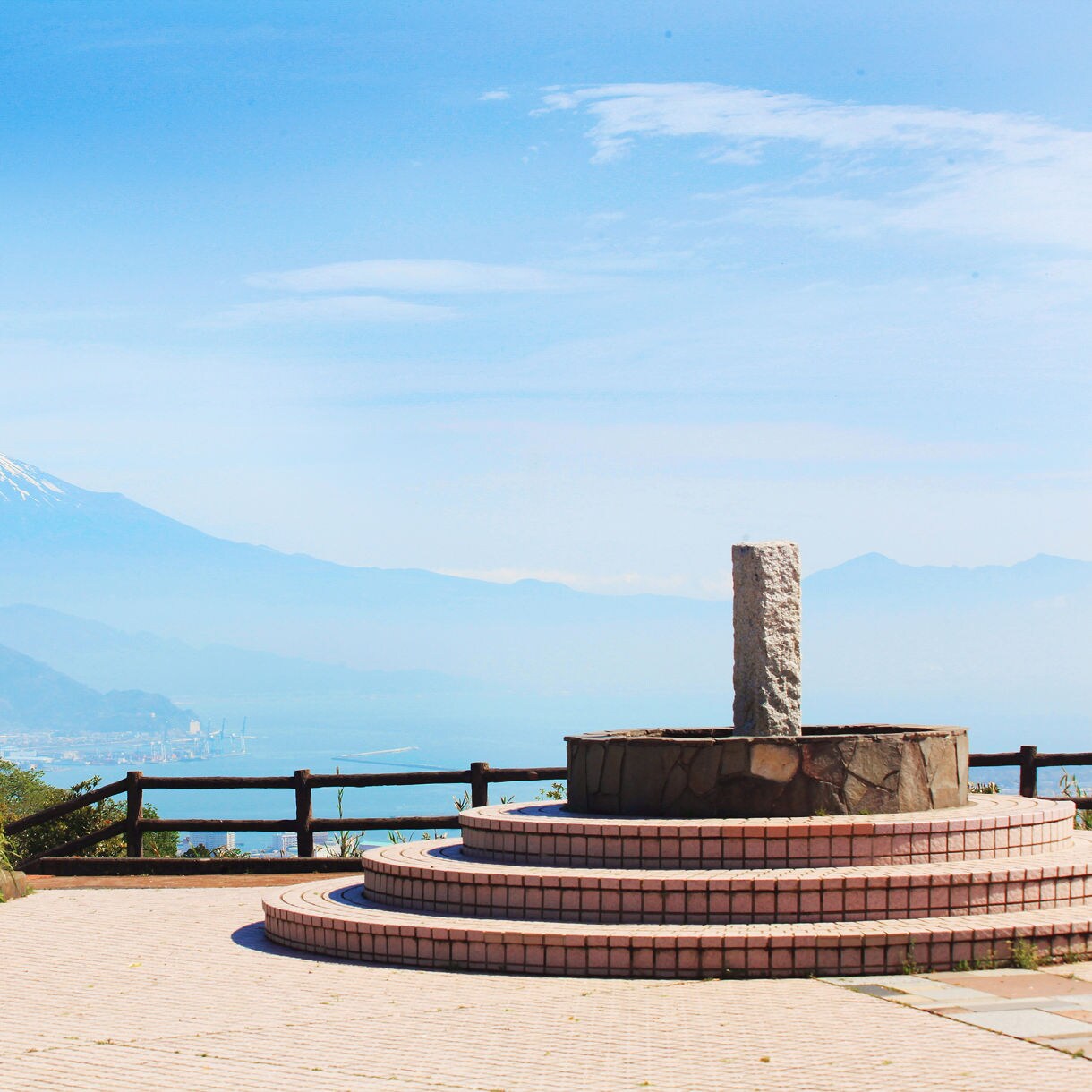 Circular stone platform at a lookout point with Mount Fuji in the distance under a clear blue sky.