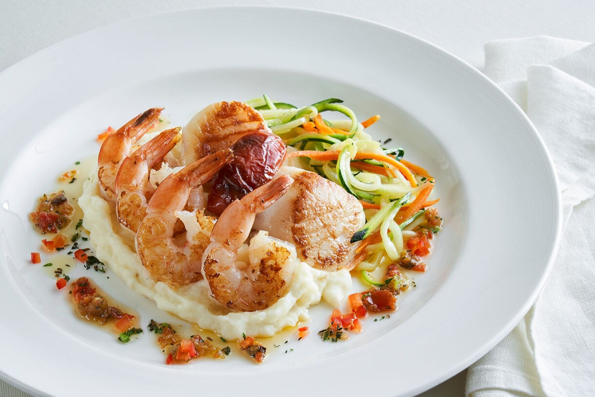 Seared shrimp served over whipped mashed potatoes with spiralized zucchini, carrots, and diced red pepper on a white plate.