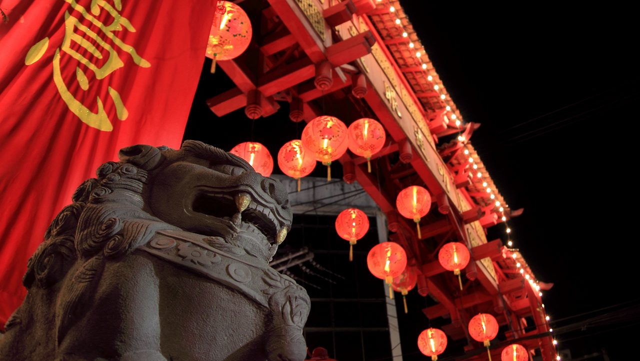 lion statue beneath gate illuminated by lanterns