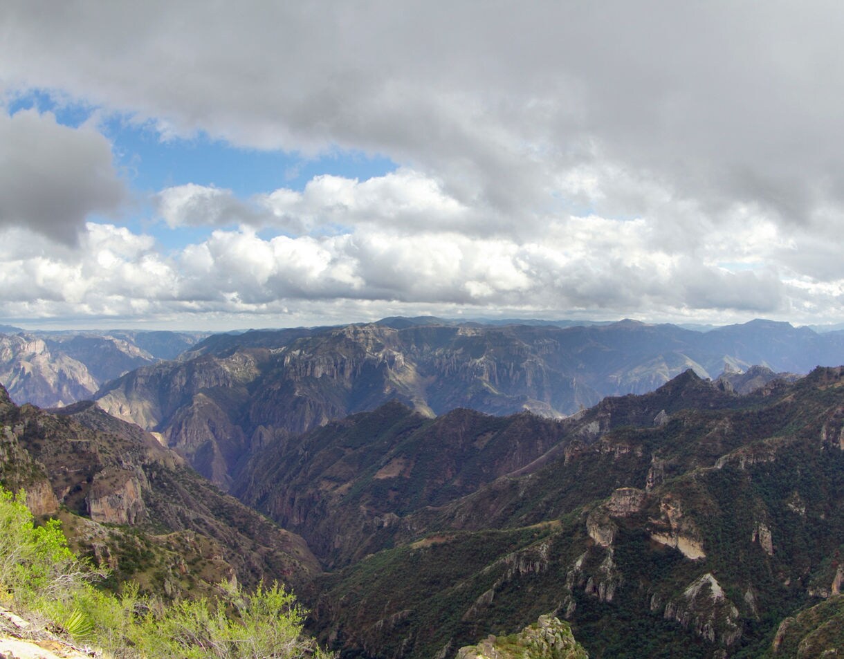 Expansive view of the Sierra Madre mountains with deep canyons and rugged cliffs beneath a dramatic sky filled with thick clouds.