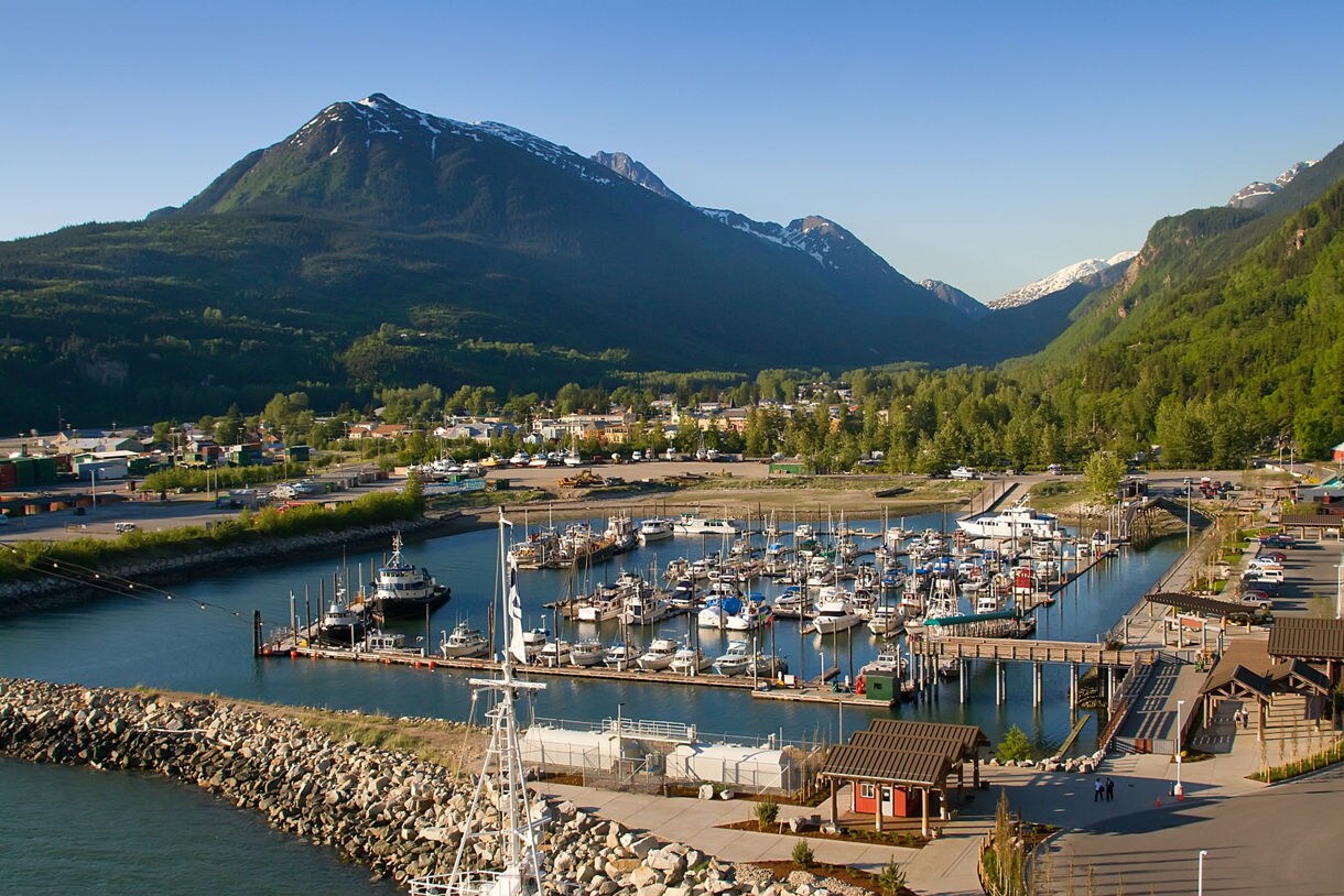 An aerial view of Skagway, Alaska, showcasing its colorful historic buildings, vibrant streets, and surrounding forested mountains under a cloudy sky.