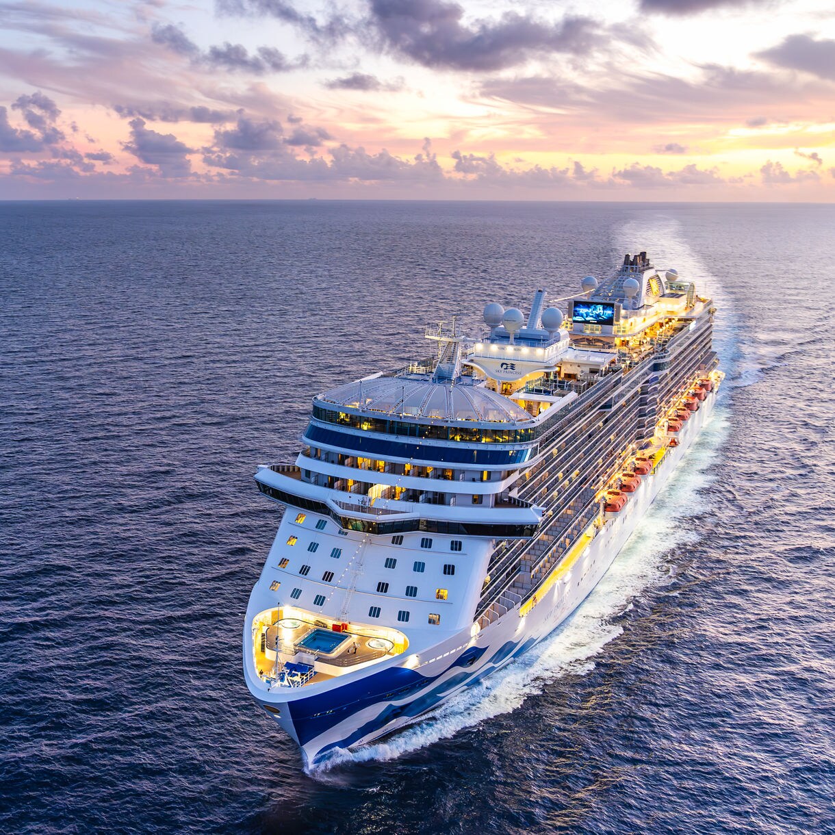 A large modern cruise ship travels across a vast ocean under a vibrant sunset sky. The vessel is illuminated with lights, creating a lively and inviting atmosphere. The scene features calm waters, dramatic clouds, and a warm color palette, emphasizing relaxation and adventure. No visible text or numeric values are present on the ship.