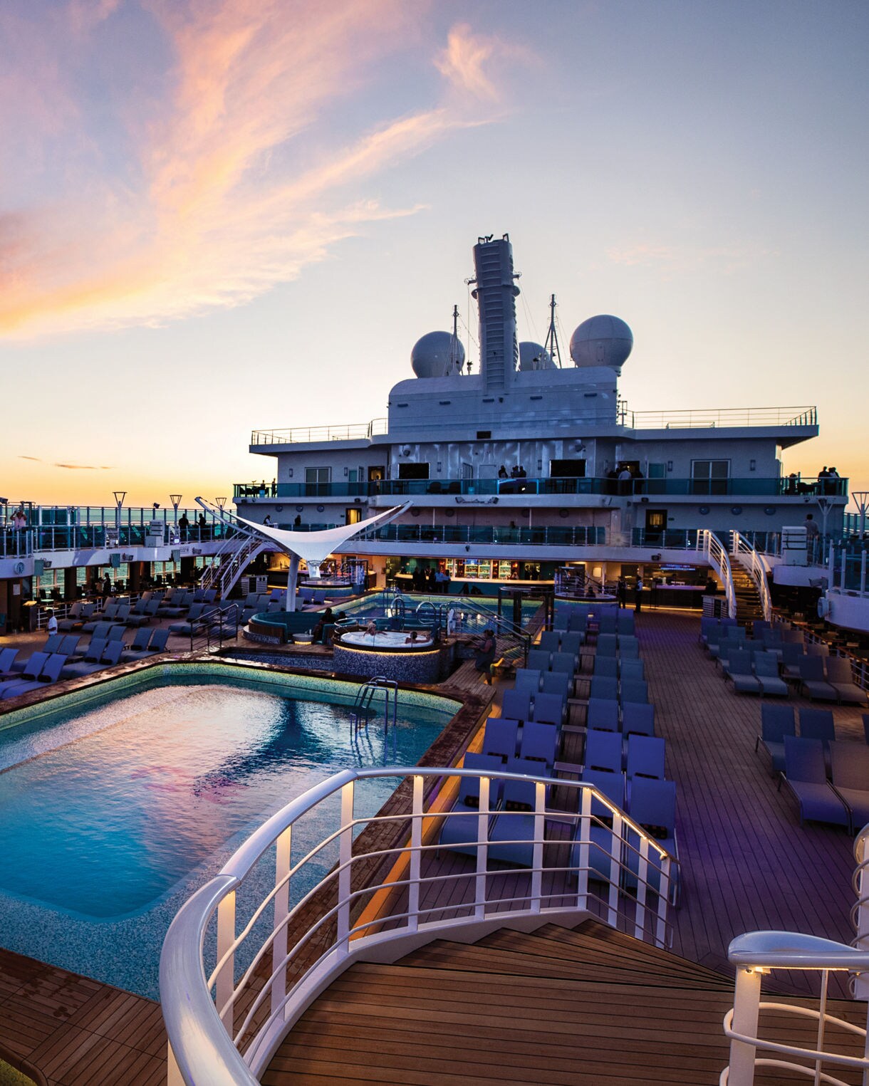 Sunset view of the pool deck on a Princess Cruises ship, featuring a spacious pool, loungers, and an elegant ship structure against a colorful sky.