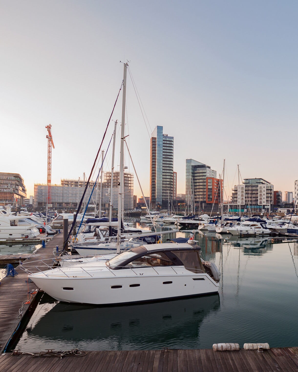 Ocean Village Marina in Southampton, England, featuring a serene harbor with yachts and boats docked alongside modern waterfront buildings. The calm waters reflect the boats and the skyline, creating a peaceful atmosphere. In the background, the skyline is a mix of contemporary architecture with glass-fronted buildings.