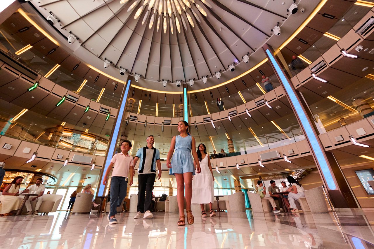 A smiling family walking through the beautiful Piazza of a Princess® cruise ship.