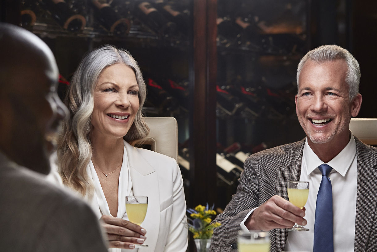 Two elegantly dressed guests smiling and raising glasses of wine at a formal dining table aboard the ship.