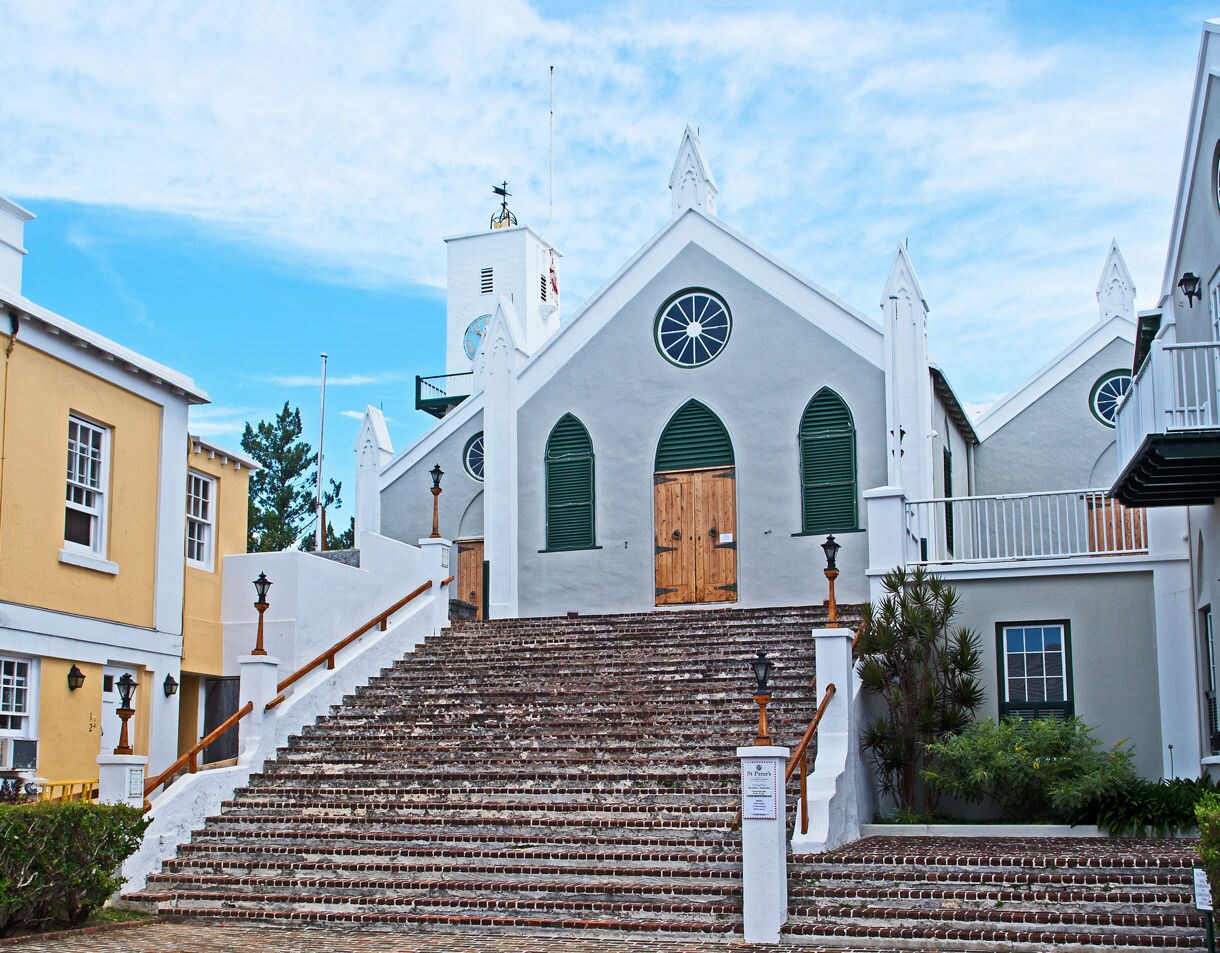 Wide stone staircase leading to the gray and white facade of Their Majesties Chappell in Bermuda, featuring arched windows and wooden doors.