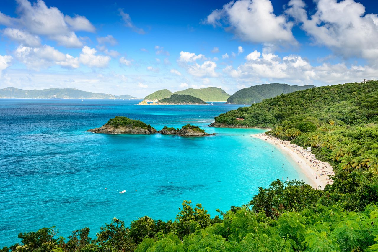 Scenic view of a Caribbean beach with turquoise waters, lush green hills, and a bright blue sky.