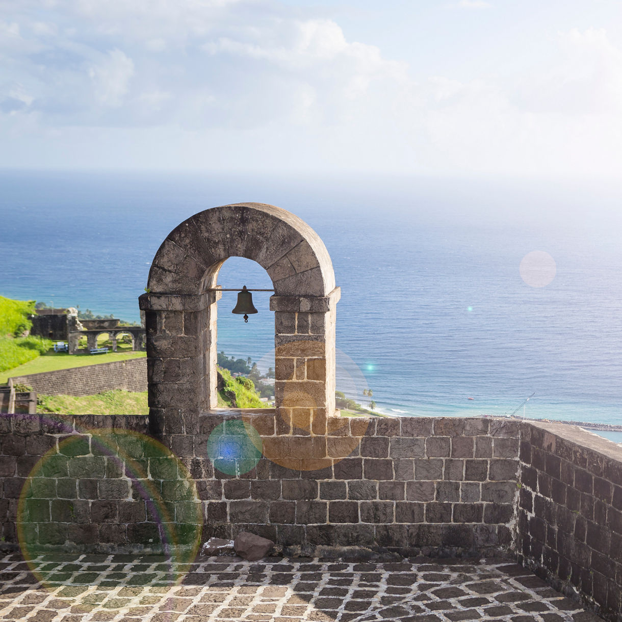 A bell tower at Brimstone Hill Fortress on St. Kitts stands against the backdrop of the ocean, surrounded by lush greenery and clear skies.