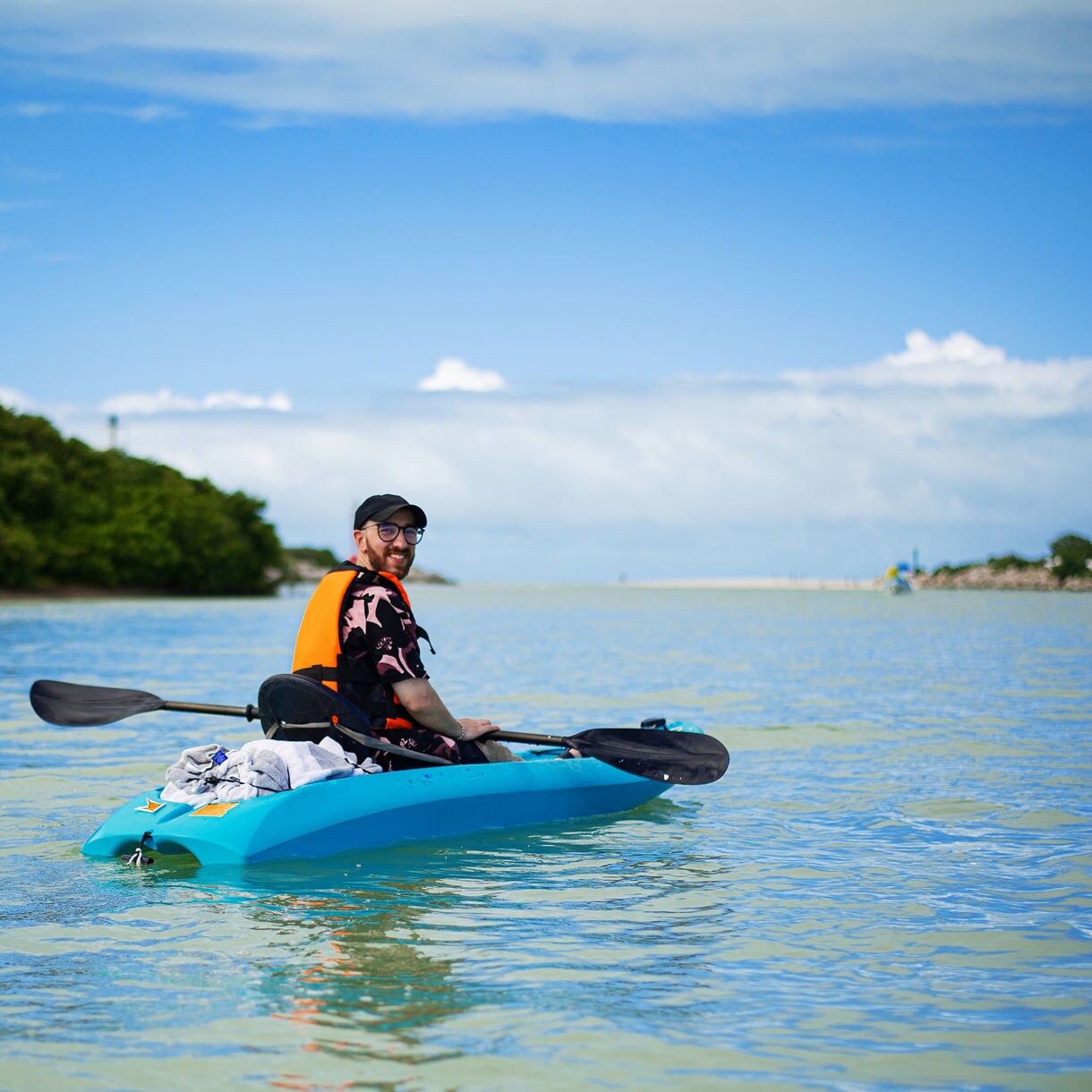 A person kayaking in the calm waters off the coast of St. Kitts, surrounded by green hills and a clear blue sky.