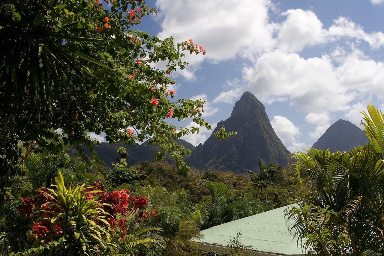 A dramatic pointed mountain peak rises above dense tropical vegetation under a partly cloudy sky
