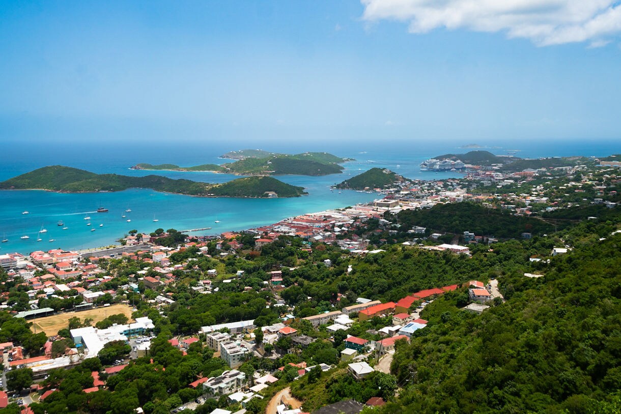A panoramic view of St. Maarten shows turquoise bays, lush green hills and small islands dotted with boats under a bright sky.