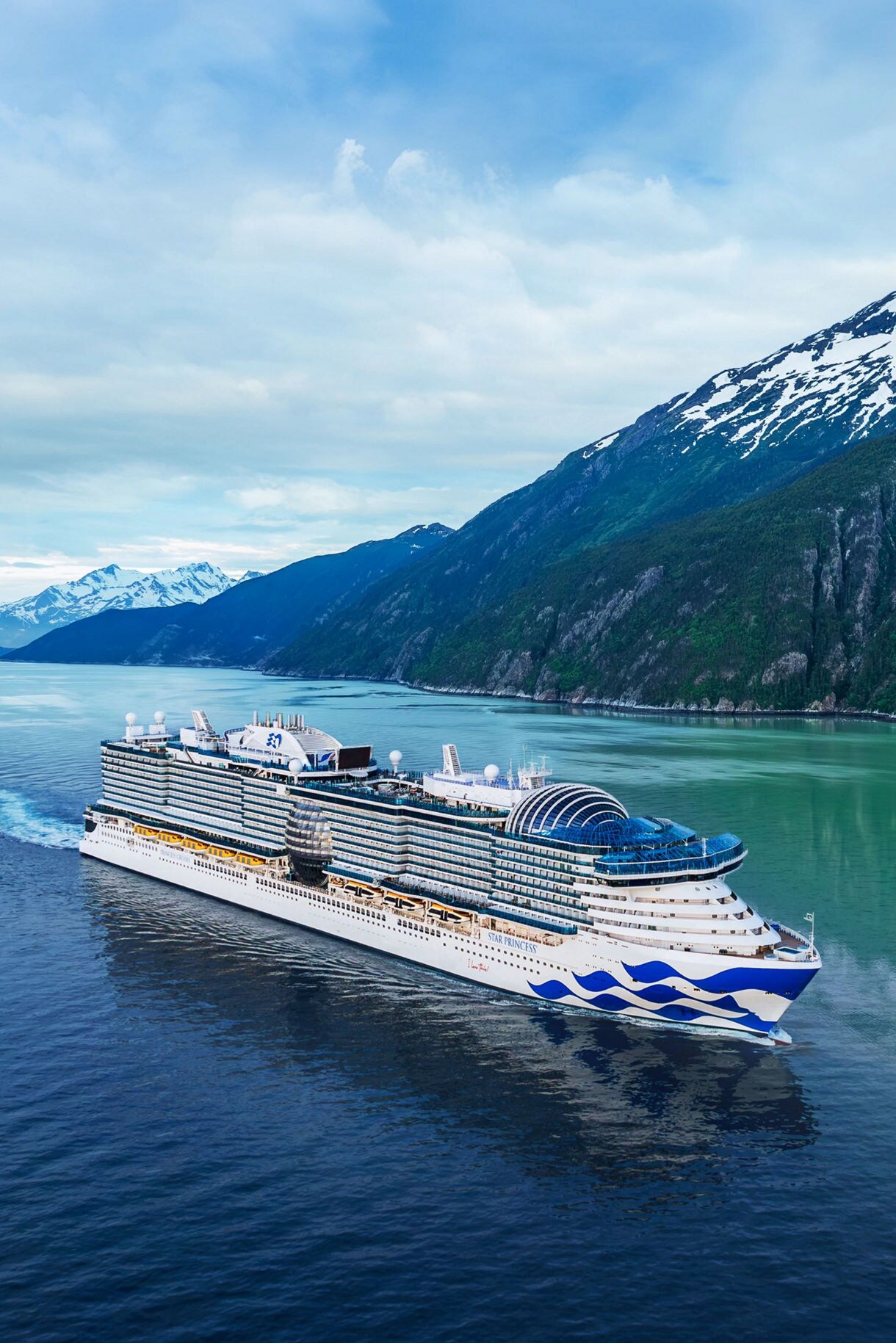 The Star Princess cruise ship sails through the scenic waters of Alaska, surrounded by towering snow-capped mountains and tranquil, glacial waters.