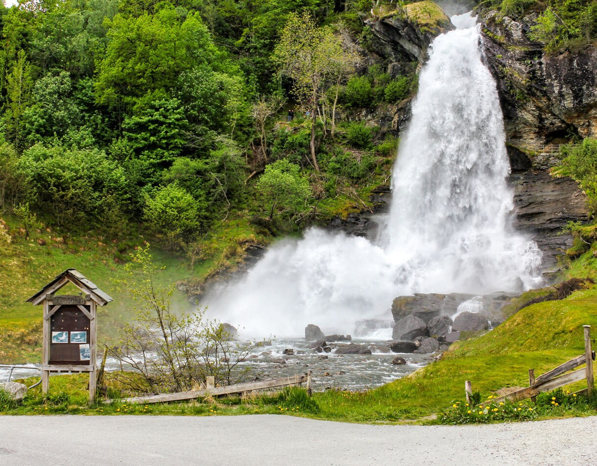 Wide waterfall crashing into rocks and river at Steinsdalsfossen, surrounded by greenery and walking paths.