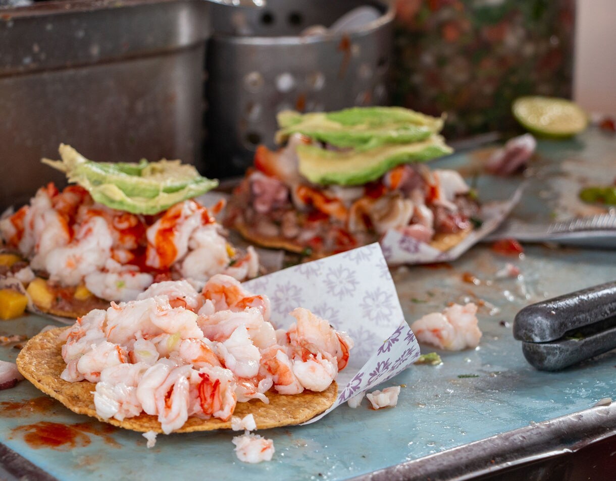 Close-up of street-style seafood tostadas in Ensenada topped with shrimp, octopus, avocado slices and hot sauce on crispy tortillas.