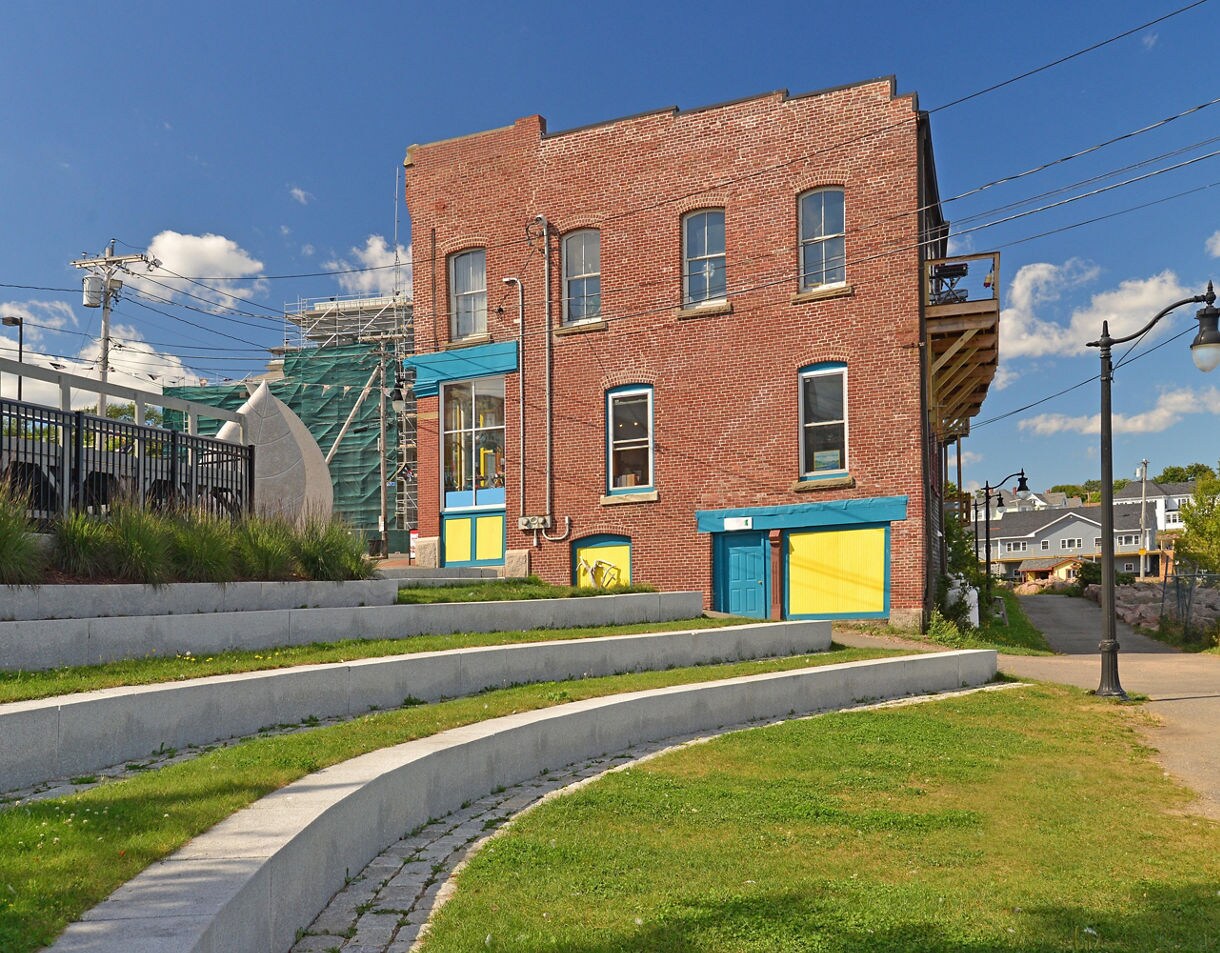 Tiered stone seating leading to a brick building with bright blue and yellow doors on a clear day in Eastport, Maine.