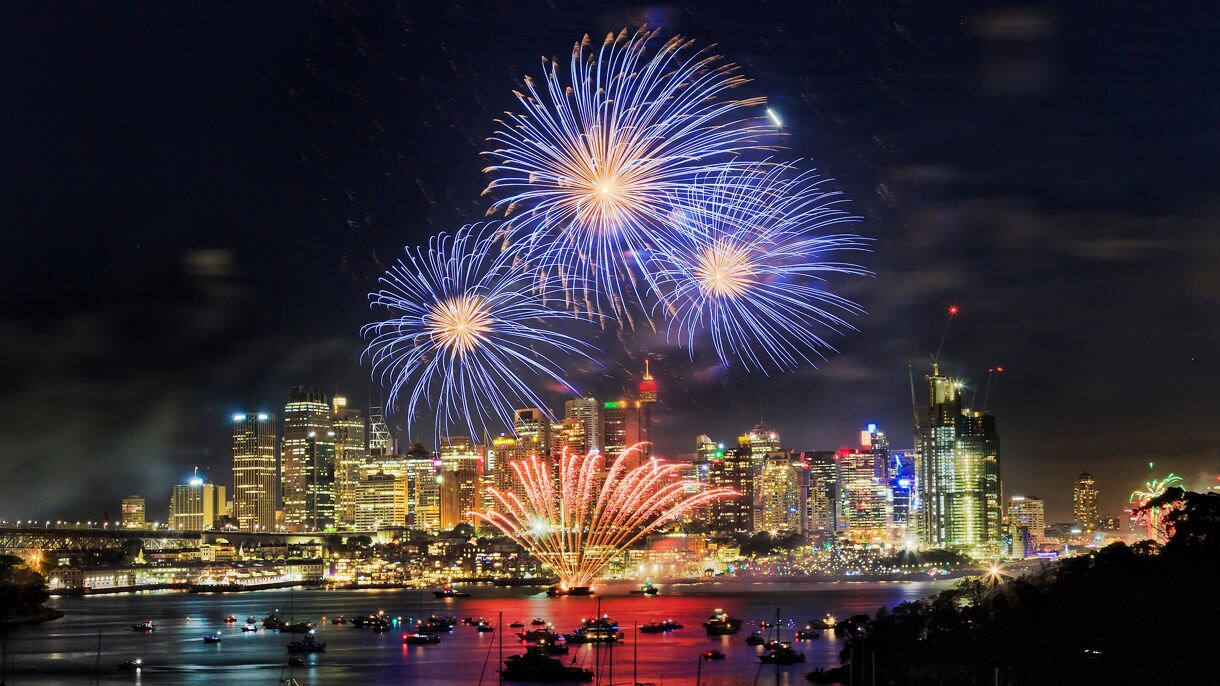 Boats in harbor viewing fireworks above city