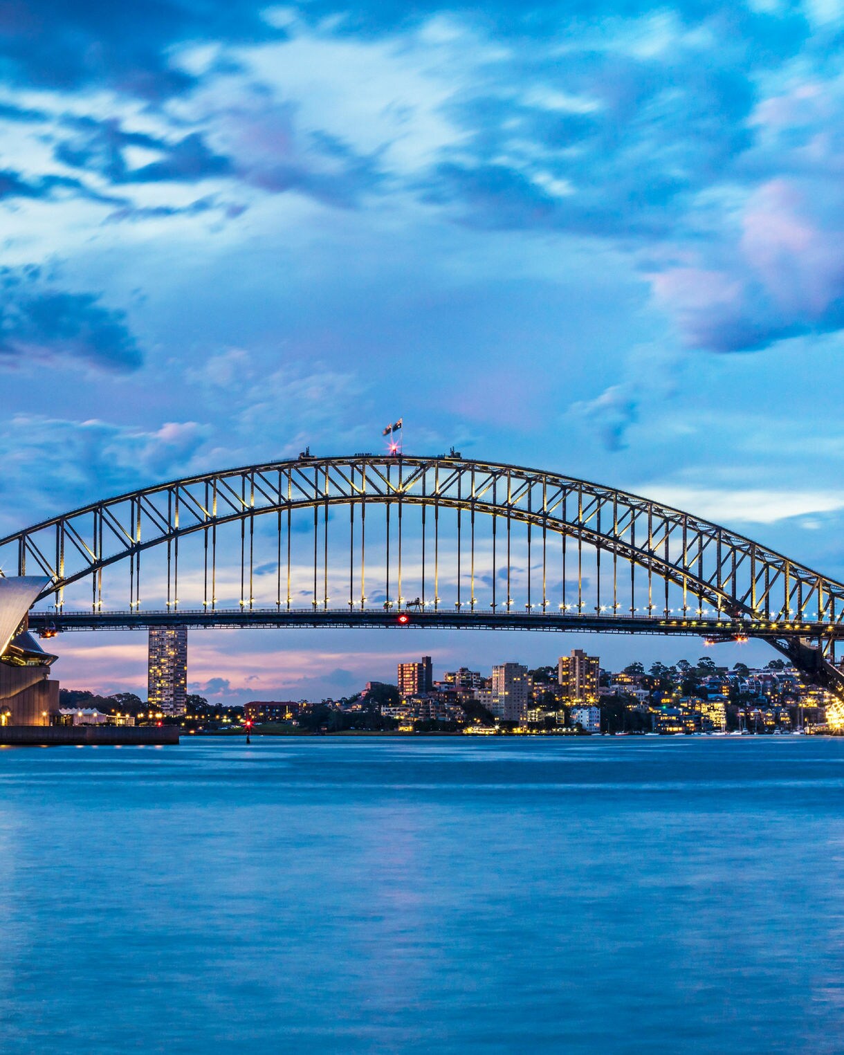 Nighttime view of Sydney Harbour in Australia, with the Sydney Opera House and Harbour Bridge beautifully lit against the dark sky, reflecting on the water below.