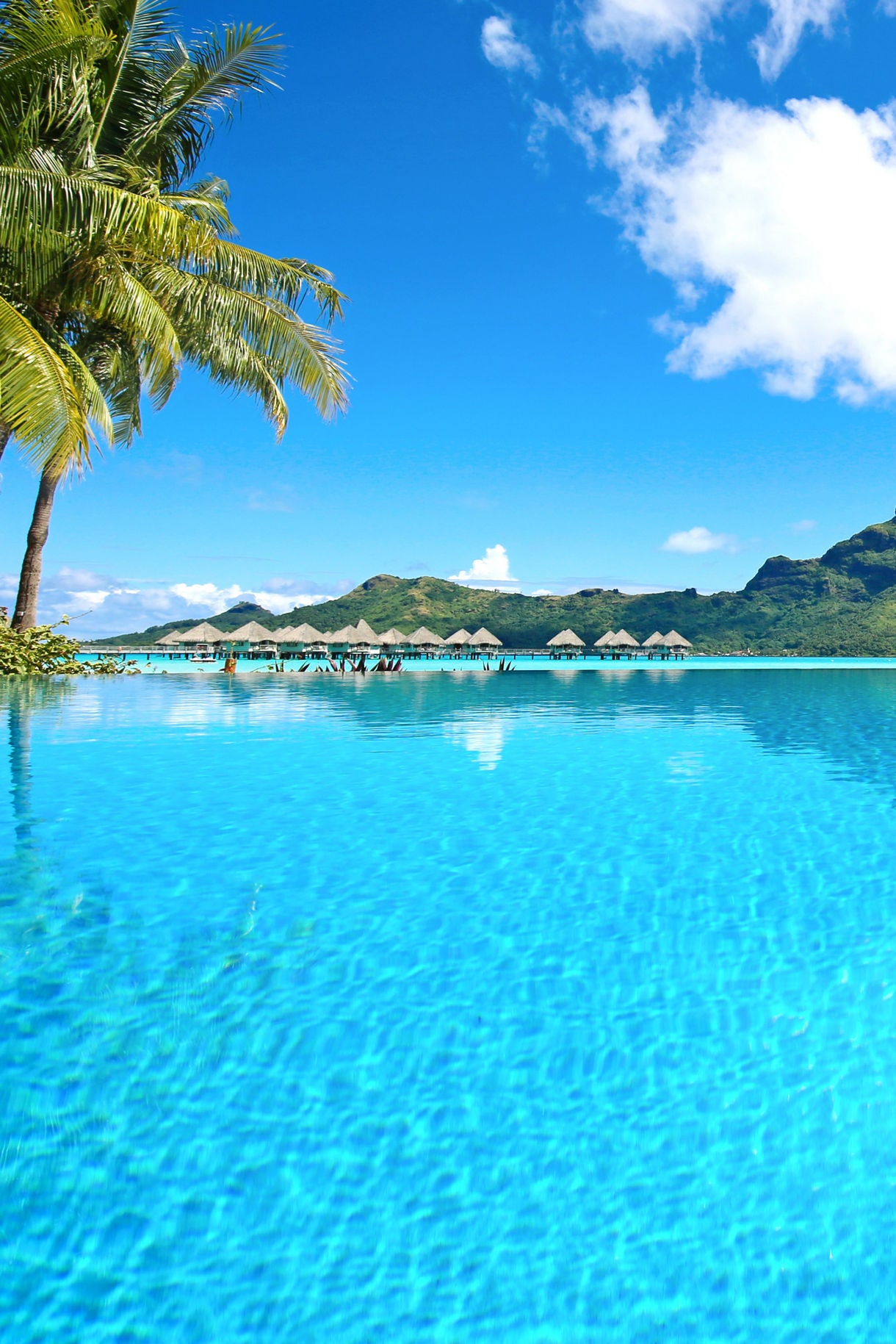 Scenic view of a luxury resort in Bora Bora, French Polynesia, featuring overwater bungalows surrounded by clear turquoise waters and lush tropical greenery.