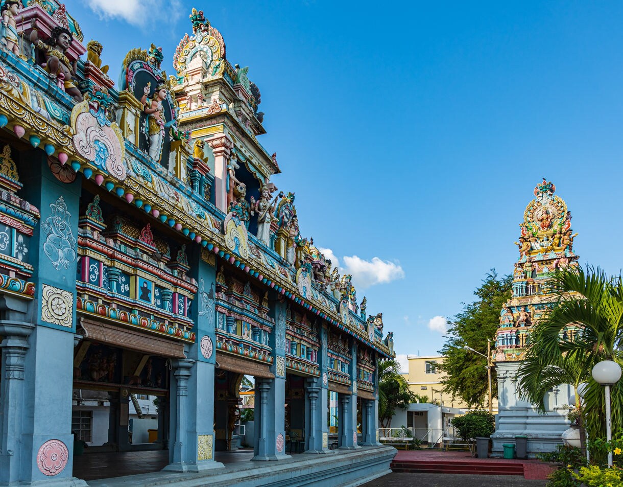 A colorful Tamil temple with intricate carved figures and bright decorative details against a clear sky.