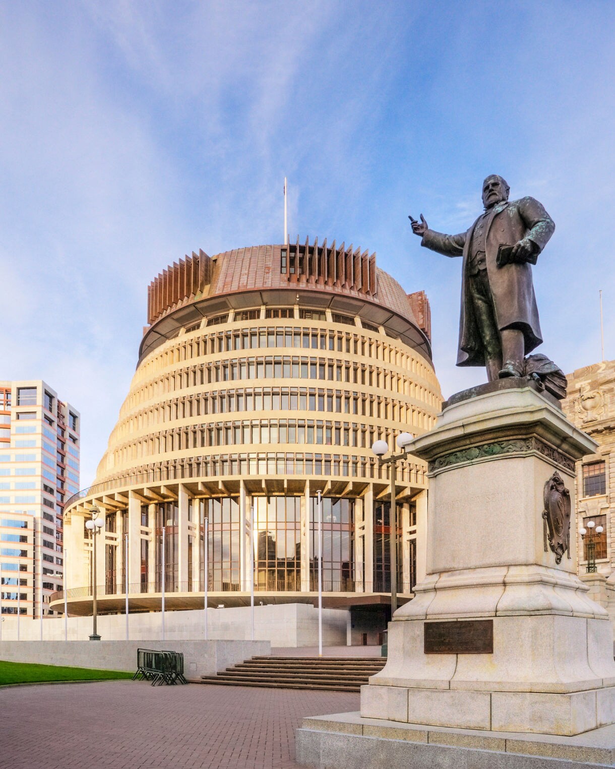The Beehive building in Wellington with a bronze statue in the foreground under a soft morning sky.
