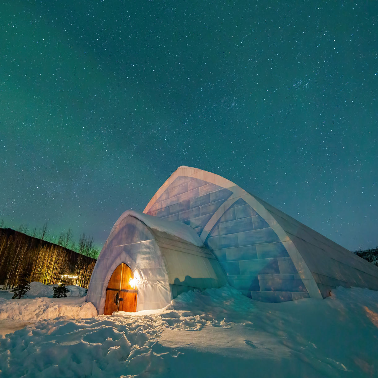An illuminated ice structure surrounded by snow beneath a starry night sky.