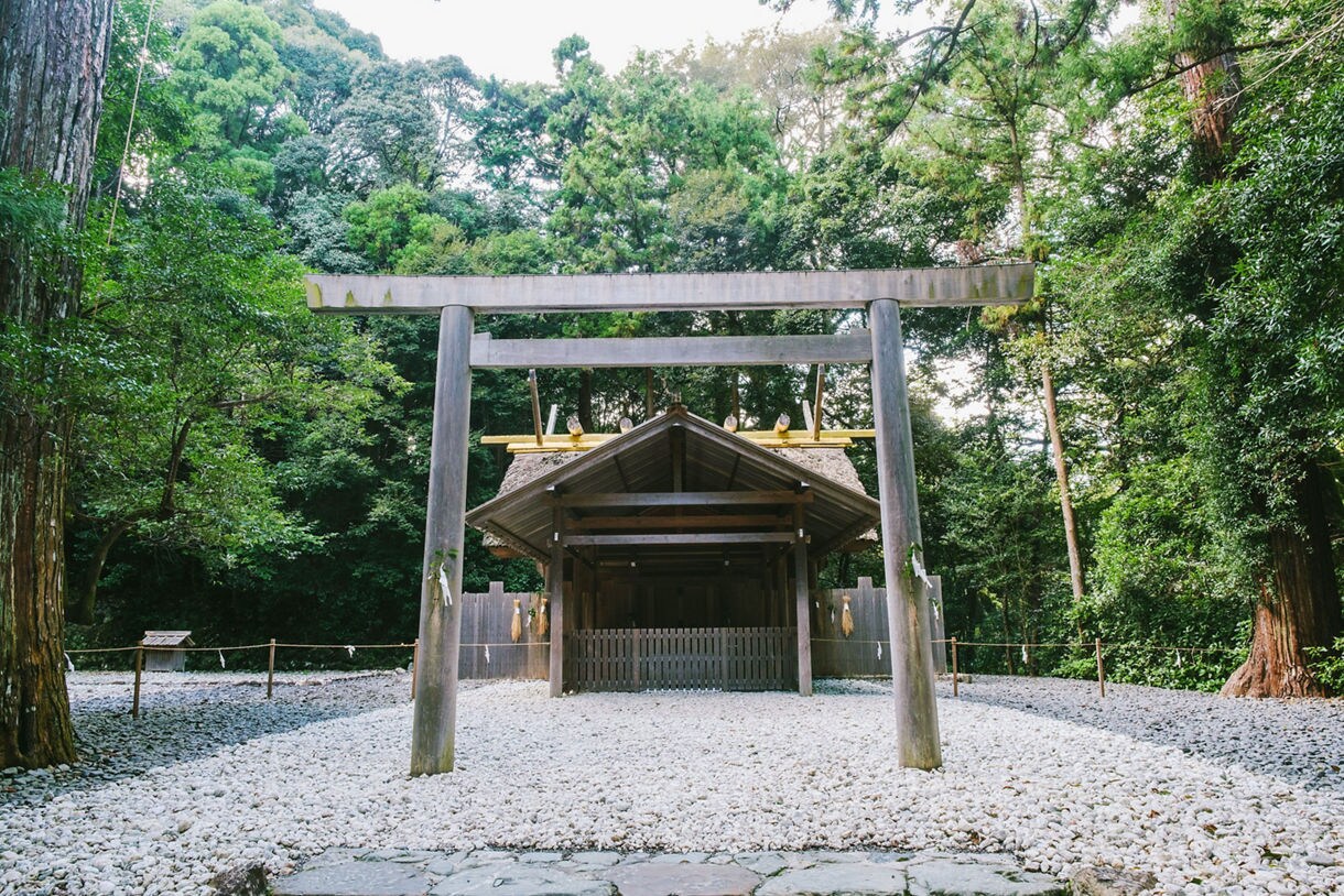Wooden torii gate and shrine building at Ise Jingu, surrounded by tall trees and white gravel.