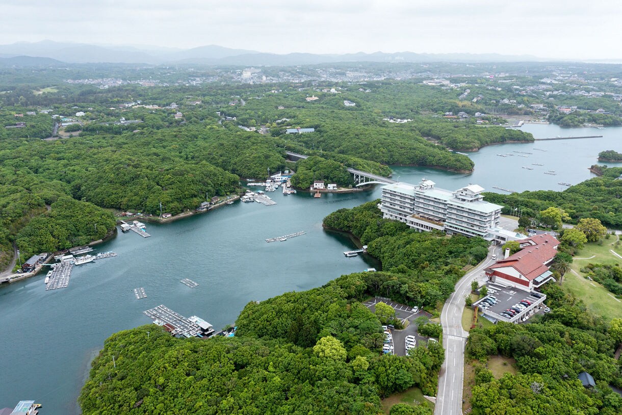 Aerial view of Ago Bay in Toba, Japan showing forested islands, pearl farming rafts and coastal resorts surrounded by calm blue water.