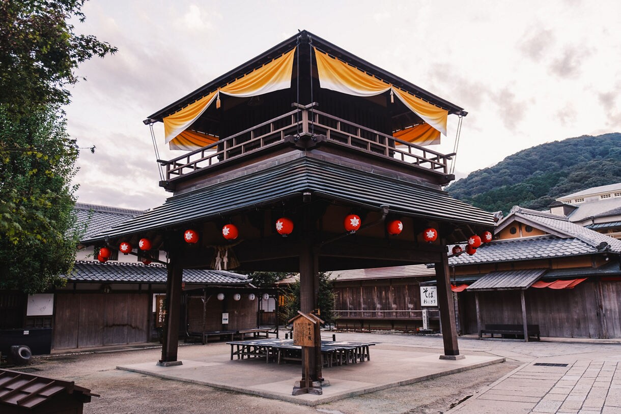 Traditional wooden pavilion with red lanterns and yellow drapes in a historic Japanese shopping street.