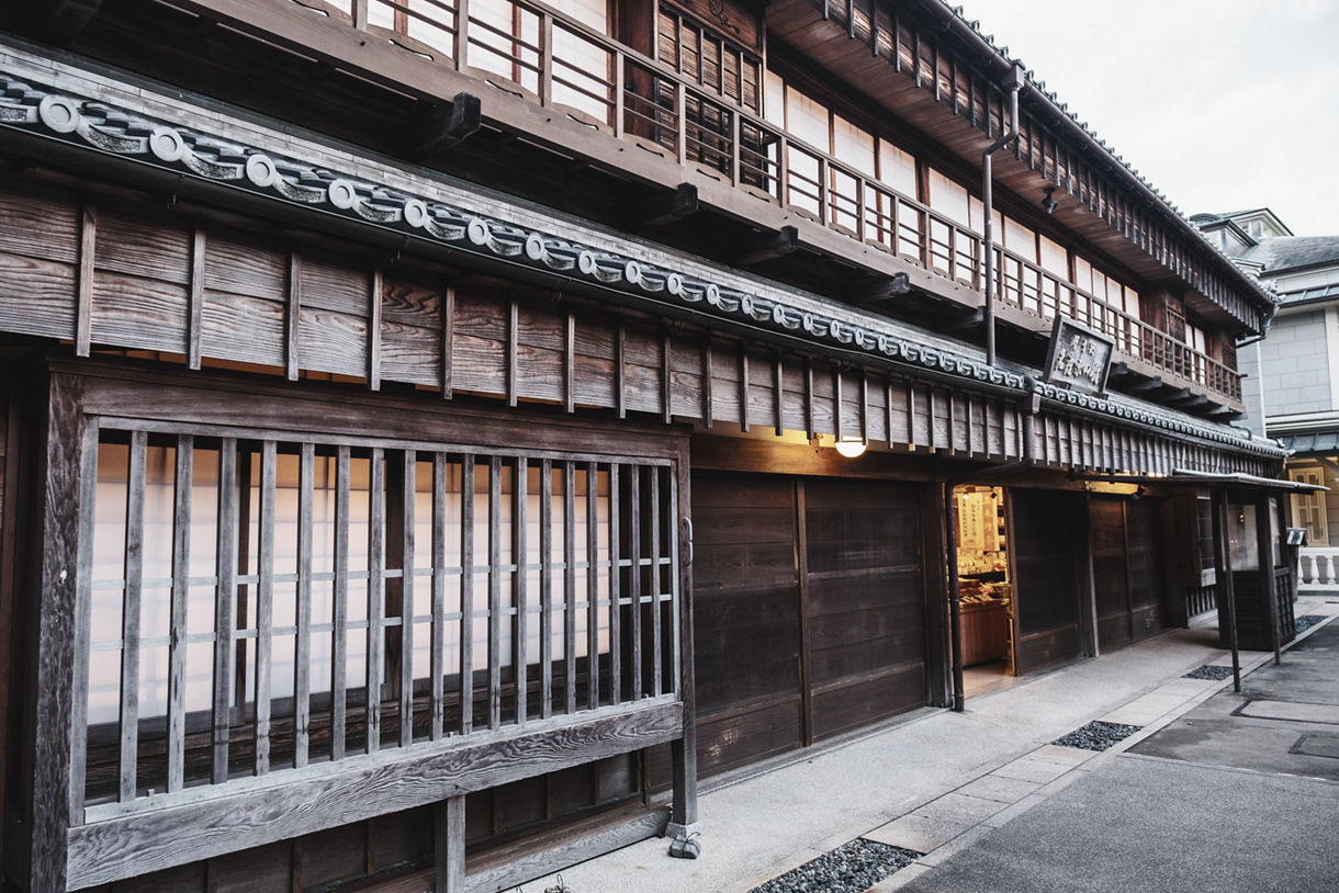 Traditional wooden building with lattice windows and a tiled roof in Okage Yokocho, Toba, lit warmly from inside.
