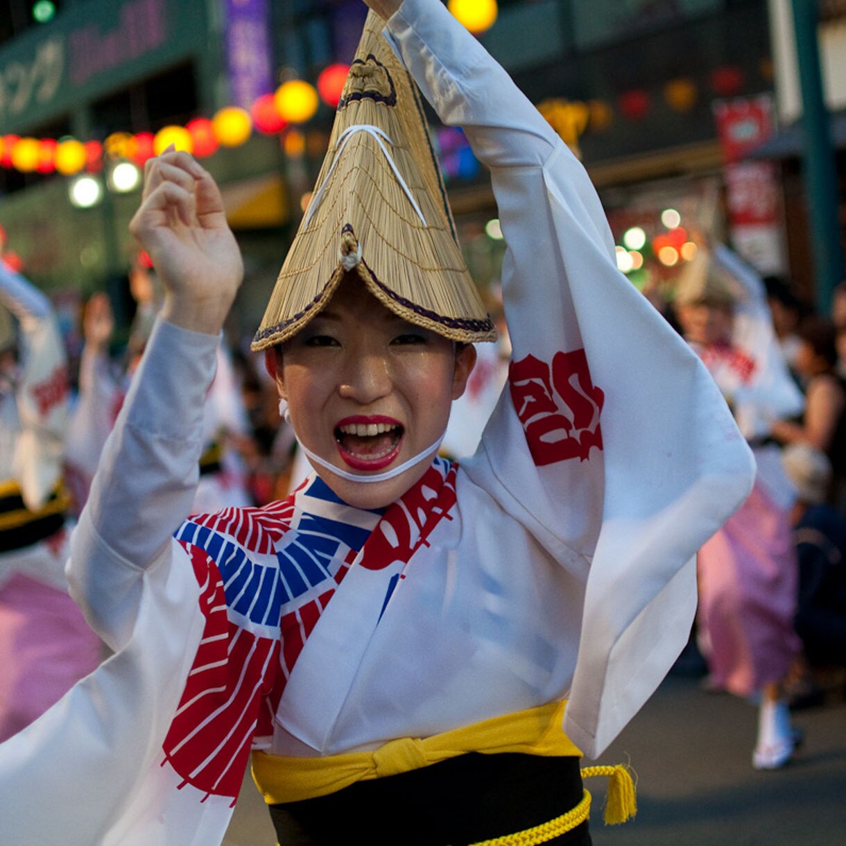 Dancers in straw hats and colorful yukata performing Awa Odori in a lively street parade.