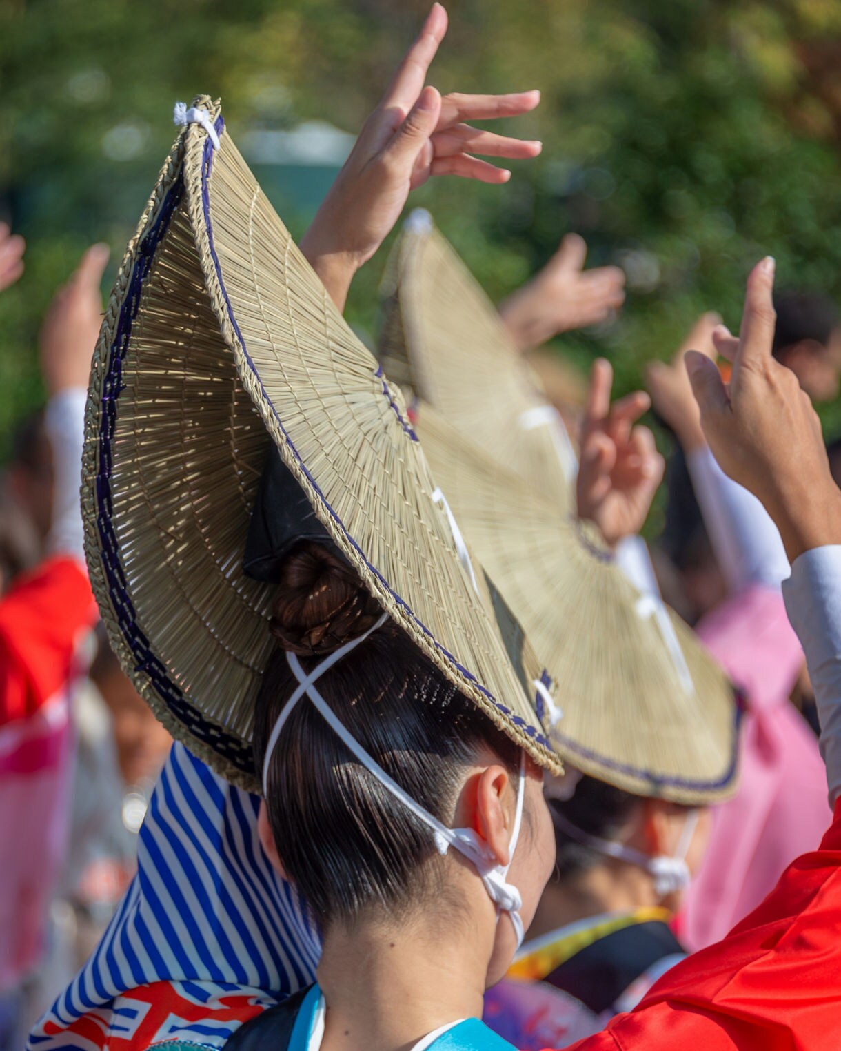 Close-up of dancers in straw hats and colorful yukata raising hands mid-performance.