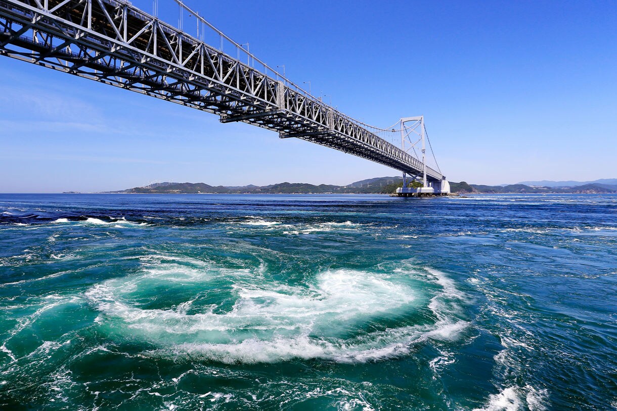 Large ocean whirlpools swirl under a long suspension bridge in Tokushima.