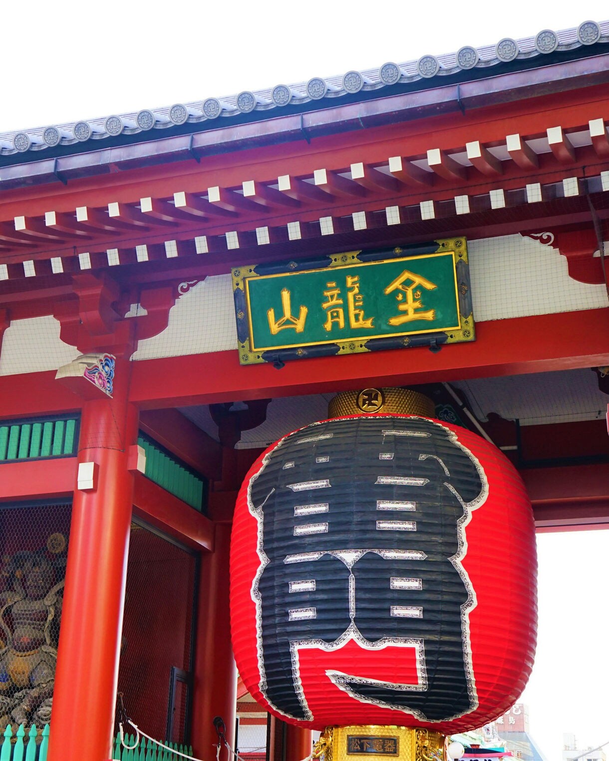 Close-up view of the iconic red paper lantern hanging at Kaminarimon, the outer entrance to Senso-ji Temple in Tokyo, with traditional Japanese architecture and signage above.