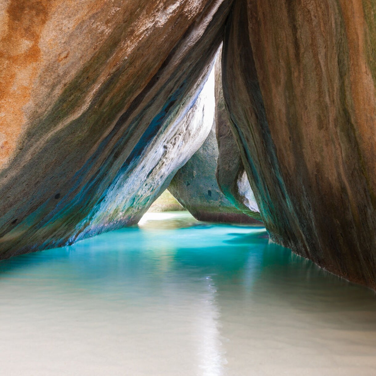 A person standing in shallow turquoise water surrounded by massive boulders, forming a picturesque cave-like structure at the Baths on Virgin Gorda.