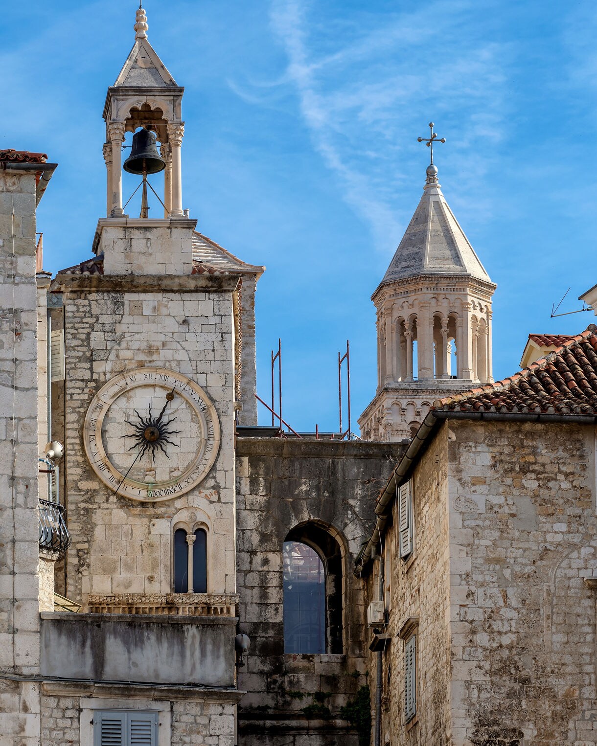 Historic clock tower and church bell tower in Split, Croatia, rising above old stone buildings under a bright blue sky.