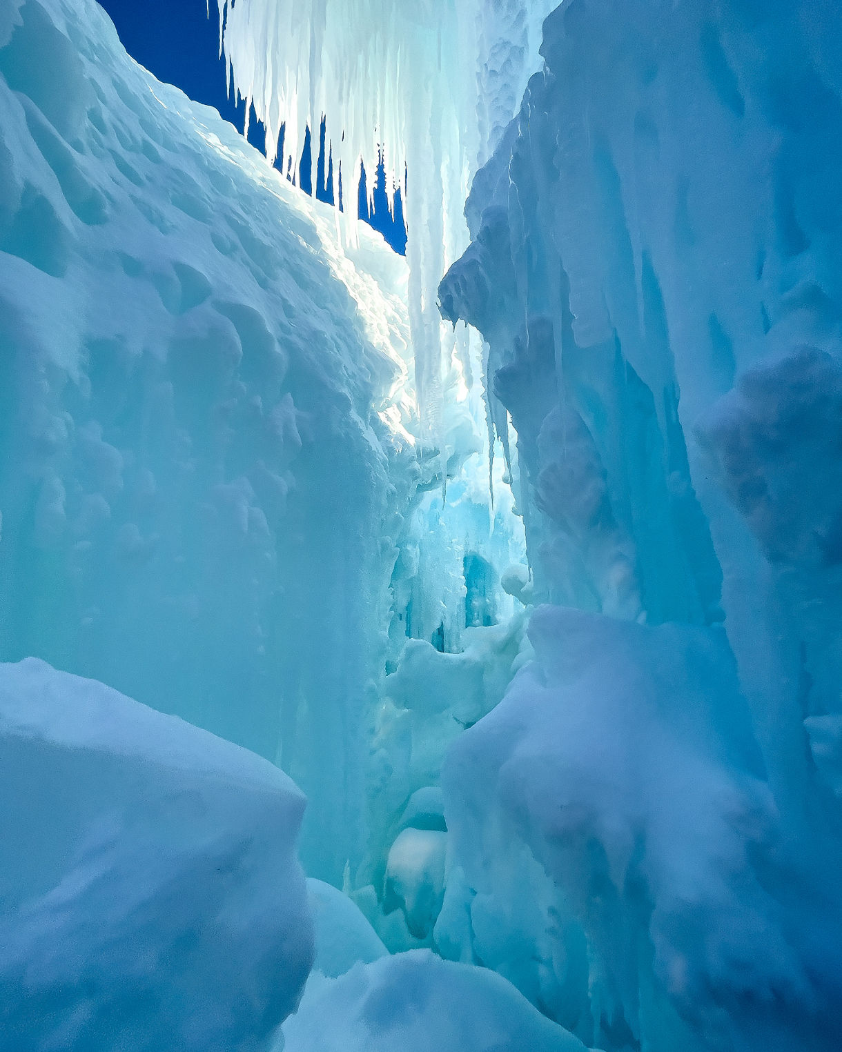 View inside a narrow glacier crevasse, with smooth blue ice walls and large icicles hanging from above.