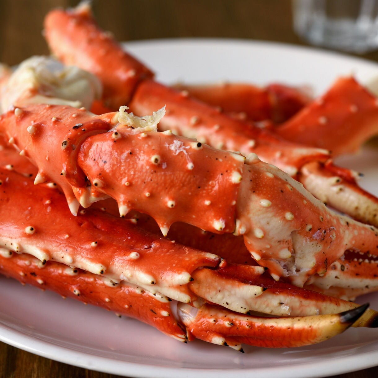 Close-up of cooked Alaskan king crab legs on a white plate with lemon wedges.