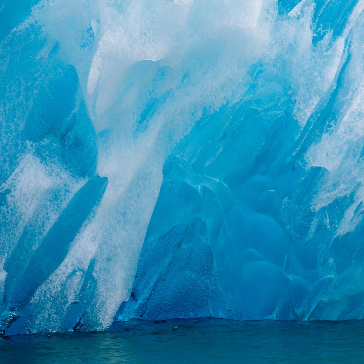 Close-up view of the South Sawyer Glacier’s deep blue ice face, showing jagged textures and icy ridges above dark green water.