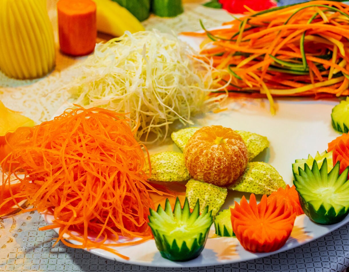 Plate of intricately carved fruits and vegetables including cucumber, carrot and orange slices arranged in decorative patterns.