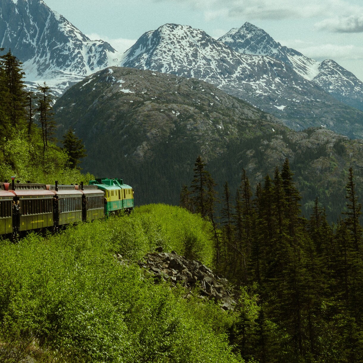 A train traveling along the White Pass & Yukon Route Railway, winding through lush greenery and steep mountain cliffs in Skagway, Alaska